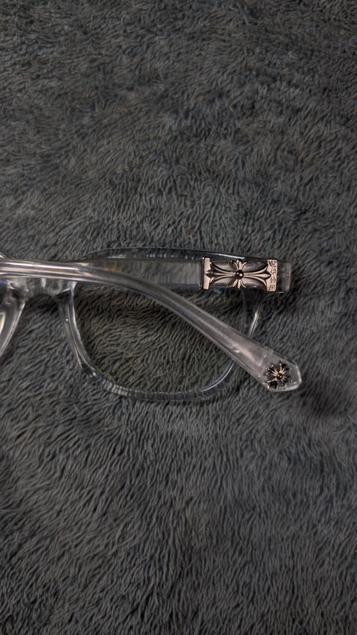 Clear eyeglasses with a decorative arm on a textured gray surface